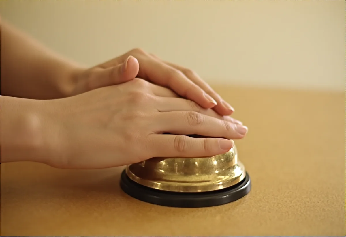 나무 카운터 위 놋쇠 종에 얹은 손, hands resting on a brass service bell on a wooden counter, 부드러운 실내 조명