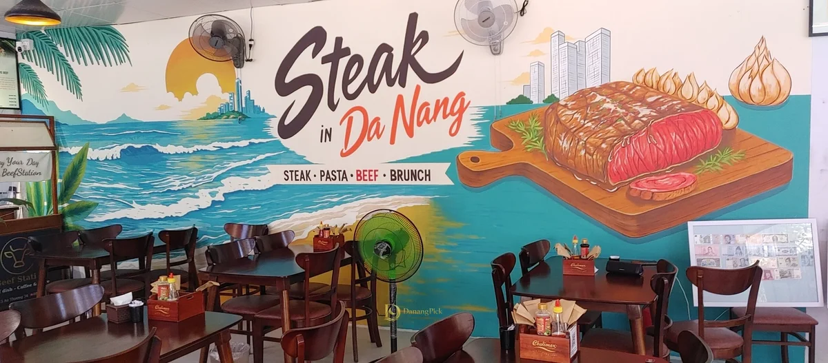 Steak in Da Nang 문구와 바다를 그린 매장 벽화, 그 앞의 원목 좌석